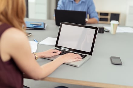 Modern business office where employees, man and woman, work on laptops and keep documents, files and mobile phones on the same shared desk